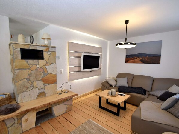 A living room with a stone wall, wooden bench, TV mounted on a wooden panel, and a sofa with cushions.