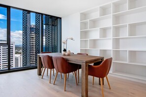 A modern dining area with a wooden table and leather chairs, a white shelving unit, and a large window with a city view.