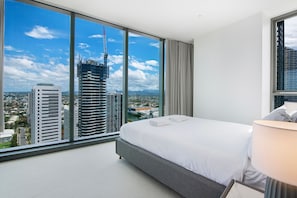 A hotel room with a large window, a bed, a lamp, and a view of the cityscape.