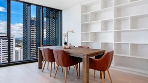 A modern dining area with a wooden table and red chairs, a white shelving unit, and a view of city buildings through large windows.