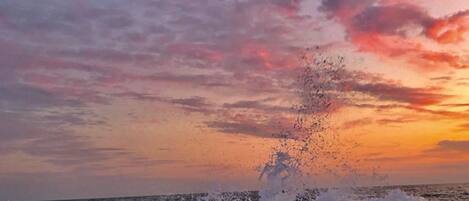 A beach with waves crashing against rocks and a sunset in the background.
