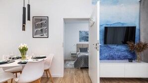 A modern room with a dining area, a bed with a blue wall mural, and a TV on a white cabinet.