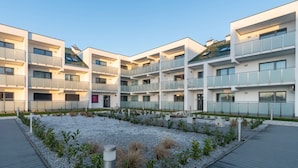 A modern multi-story residential building with balconies, a landscaped courtyard, and a clear sky.