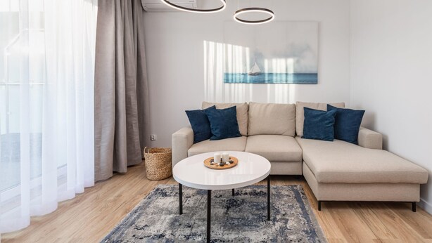 A modern living room with a beige sofa, a round coffee table, and a painting of a sailboat on the wall.