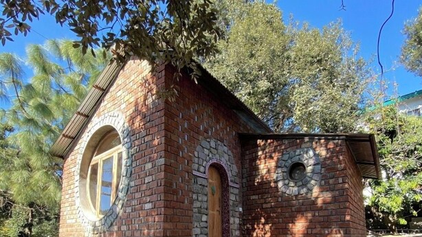 A small brick building with a wooden door and window, surrounded by a wooden deck and stone steps. - Chirping Hills Resort Bhimtal (Nainital)