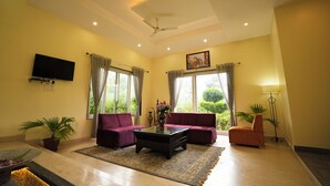 A living room with a sofa, armchair, coffee table, and potted plants. - Chirping Hills Resort Bhimtal (Nainital)