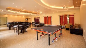 A spacious room with a ping pong table, multiple tables, chairs, and a ceiling fan. - Chirping Hills Resort Bhimtal (Nainital)