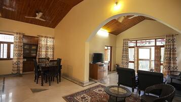 A spacious living area with a high ceiling, wooden beams, a dining table with chairs, a sofa, and a television.