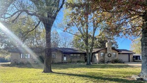 A two-story house with a stone chimney, a garage, and a well-maintained lawn. - The Ranch House (Flippin)
