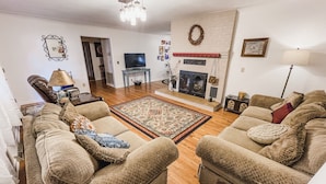 A living room with two beige sofas, a patterned rug, a fireplace, and a television. - The Ranch House (Flippin)