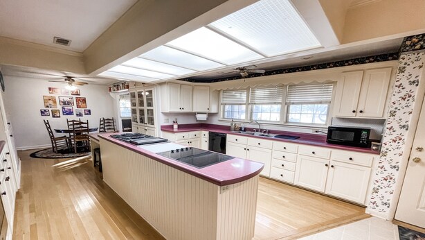 A kitchen with a central island, white cabinets, a microwave, and a window with blinds. - The Ranch House (Flippin)
