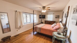 A bedroom with a four-poster bed, a ceiling fan, a dresser, and a small table with a lamp. - The Ranch House (Flippin)