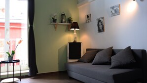 Un salon avec un canapé, une lampe, une petite table sur laquelle est posée une plante, et une fenêtre avec des rideaux.