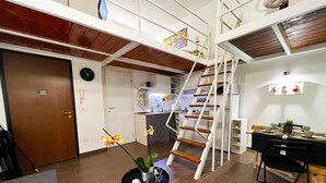 Un grand espace de vie comprenant une cuisine, une table à manger avec des chaises, un escalier et une petite table agrémentée d’une plante et d’une tasse.