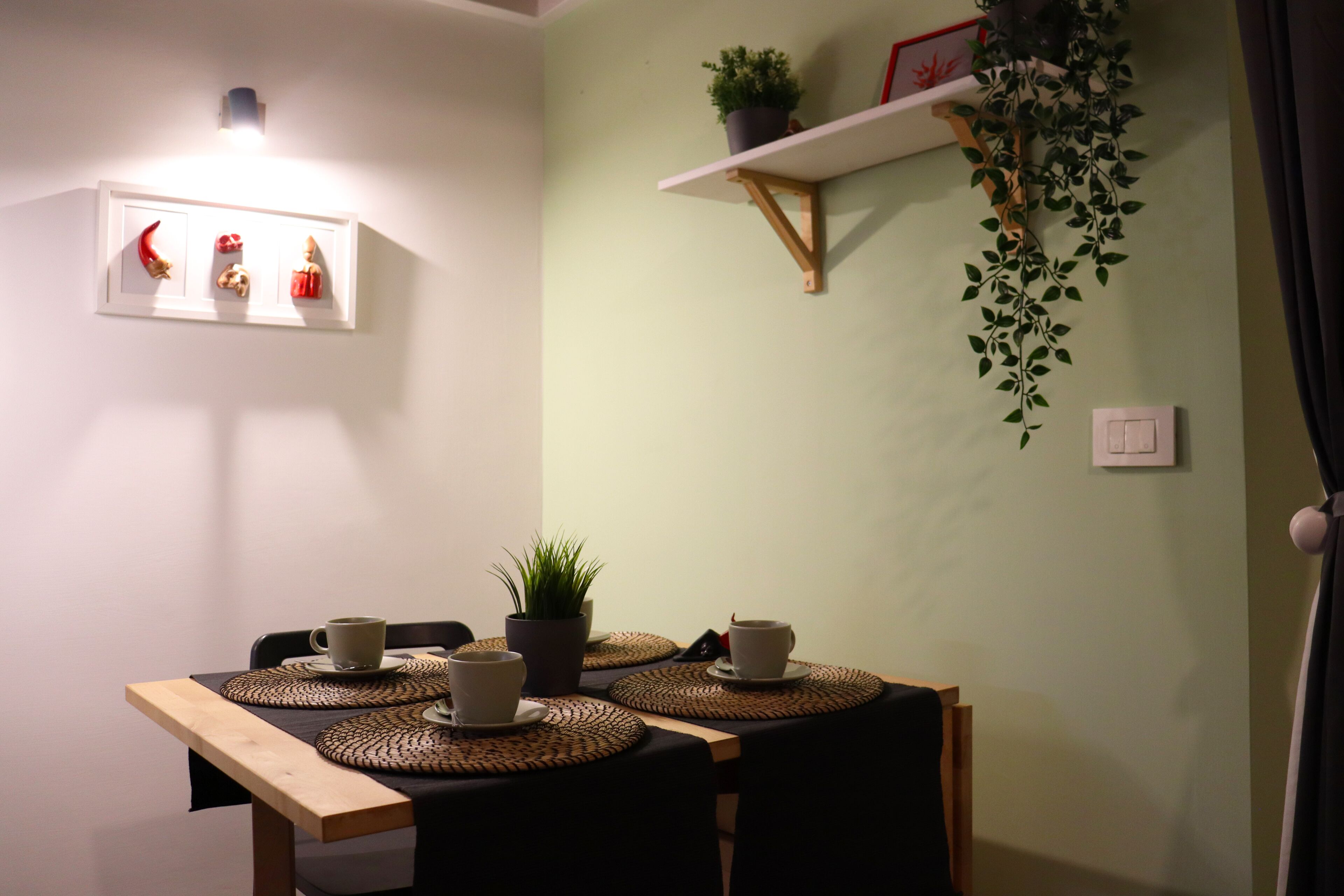 Zona de menjador amb taula preparada per a dues persones, amb sotsmajols teixits, dues tasses i una planta en test.