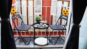 Un balcon avec deux chaises noires, une petite table ronde et un pot de fleurs.