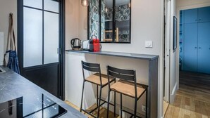 Eine kleine Küche mit schwarzem Arbeitsplatz, zwei Barhocker, einer Kaffeemaschine und einer roten Tasche auf der Arbeitsfläche.