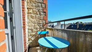 Ein kleiner Balkon mit blauem Tisch und Stühlen, einer Steinmauer und Blick auf Gebäude im Hintergrund.