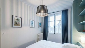 Ein Schlafzimmer mit Bett, Heizkörper, einem Fenster mit Vorhängen und gerahmten Bildern an der Wand.