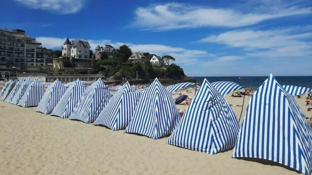 Ein Strand mit gestreiften Sonnenschirmen und einem Gebäudekomplex im Hintergrund.