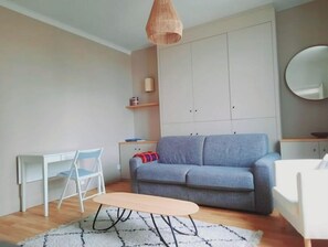 Uma sala de estar moderna com um sofá cinzento, uma pequena escrivaninha branca e um candeeiro suspenso.