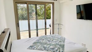 Un dormitorio con una cama, un televisor montado en la pared y un ventanal corredero que da a un espacio exterior.