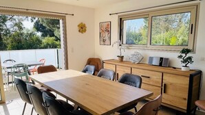 Un comedor con una mesa y sillas de madera, un mueble de madera y una ventana con vistas a árboles.