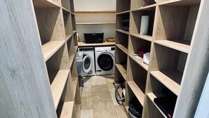 Un lavadero con dos lavadoras, estanterías de madera y suelo de baldosas.