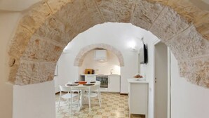 Vue intérieure d’une pièce avec une arche en pierre donnant sur un espace cuisine.