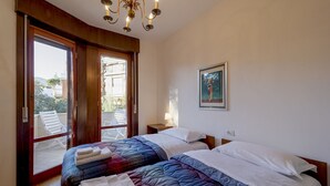 A bedroom with two beds, a balcony, a painting, and a chandelier. - GuestHost - Cozy penthouse of 110 sqm, able to accommodate up to 4 people, located on the fourth floor of a building with elevator and private garage.The apartment boasts an enchanting view of the sea and Portosole, surrounded by Villa Ormond's and Villa (Sanremo)