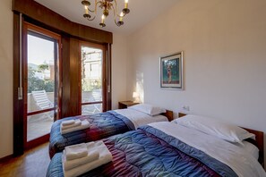 Une chambre avec deux lits, un balcon, un tableau et un lustre.