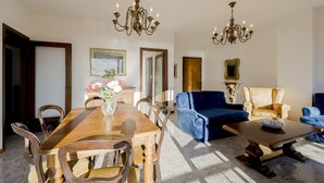 A dining area with a wooden table and chairs, a blue sofa, and a patterned armchair. - GuestHost - Cozy penthouse of 110 sqm, able to accommodate up to 4 people, located on the fourth floor of a building with elevator and private garage.The apartment boasts an enchanting view of the sea and Portosole, surrounded by Villa Ormond's and Villa (Sanremo)