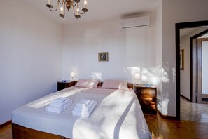 Un dormitorio con cama, mesitas de noche, una araña, un equipo de aire acondicionado y un cuadro enmarcado en la pared.