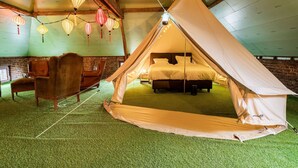 Ein Zeltenraum mit einem Bett, einem Ledersessel und hängenden Laternen.