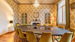 Ein Esszimmer mit einem runden Tisch, grünen Stühlen, einer Chandelüstere und blumigem Tapetenmuster.