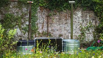 A garden with metal barrels, a brick wall, and a green hose.