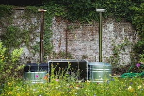 A garden with metal barrels, a brick wall, and a green hose.