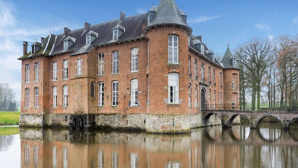 Ein großes Backsteingebäude mit zahlreichen Fenstern und einem Turm, gelegen neben einer ruhigen Wasserfläche.