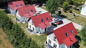Eine Reihe moderner, zweigeschossiger Häuser mit roten Dächern und großen Fenstern, umgeben von Grünflächen und einem Parkplatz.