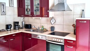 A modern kitchen with red cabinets, a stainless steel sink, a built-in oven, and a coffee maker. - Apartment in Deudesfeld With Private Terrace (Schutz)