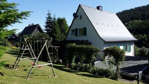 A white house with a sloped roof, a swing set, and a well-maintained lawn. - Holiday Home With Terrace in Sauerland (Brilon)