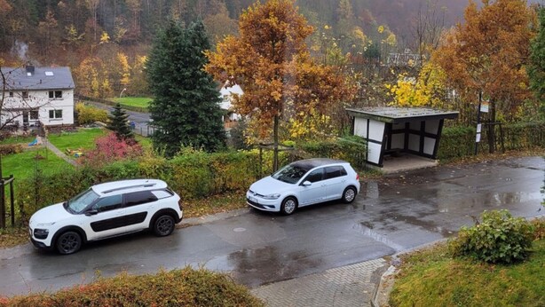 A residential area with two parked cars, a house, and a small building with a sloped roof. - Holiday Home With Terrace in Sauerland (Brilon)