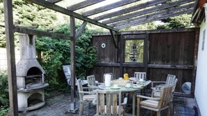 An outdoor patio with a stone oven, wooden chairs, and a table set for dining. - Holiday Home With Terrace in Sauerland (Brilon)