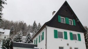 A two-story house with green shutters, a garage, and snow-covered surroundings. - Holiday Home With Terrace in Sauerland (Brilon)