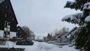 A residential street with houses on both sides, a car parked on the left, and snow on the ground. - Ferienwohnung in Winterberg am Skigebiet (Winterberg)