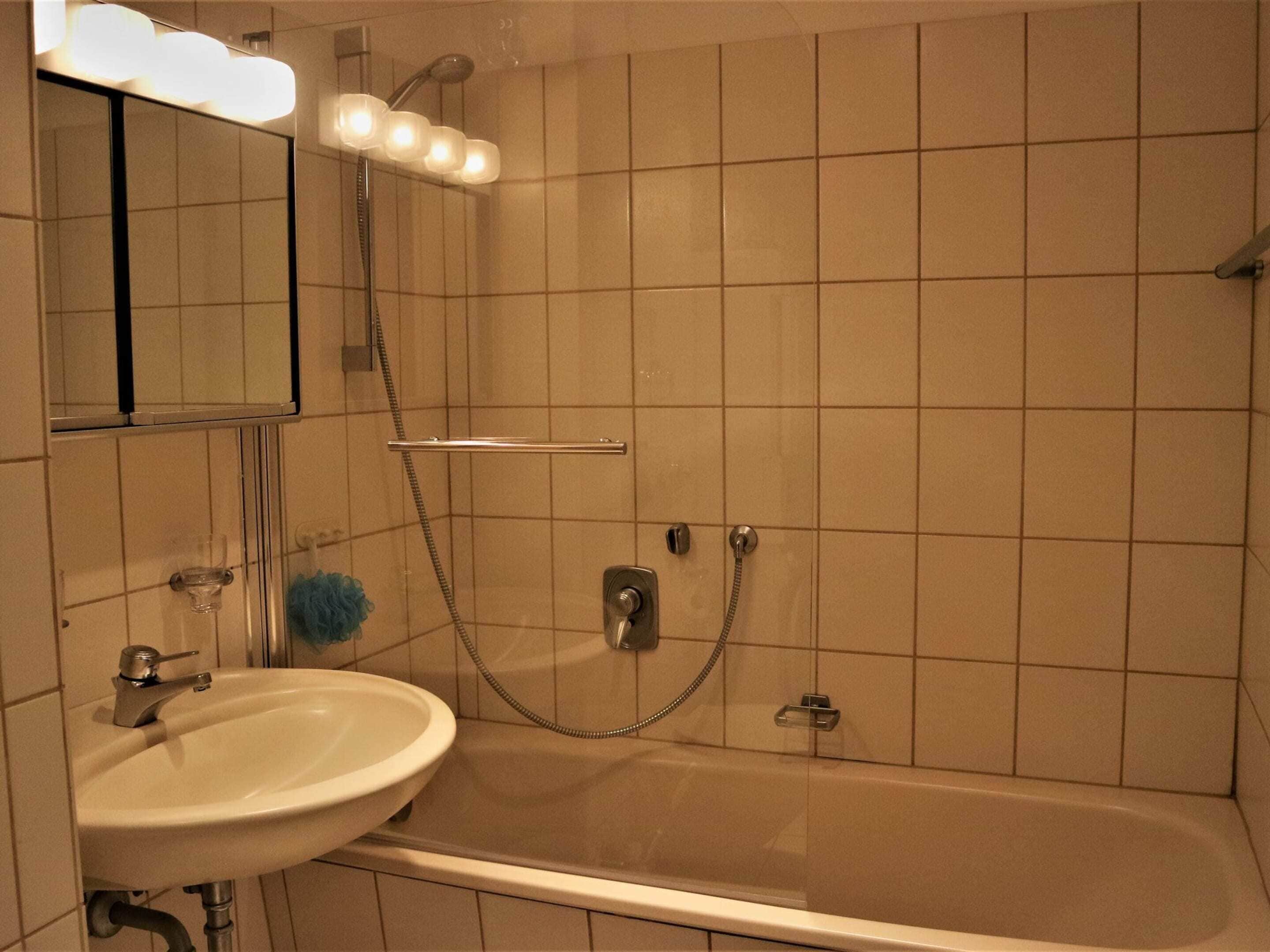 Une salle de bain équipée d’une baignoire, d’un lavabo, d’un miroir et d’une douche avec un pommeau de douche amovible.