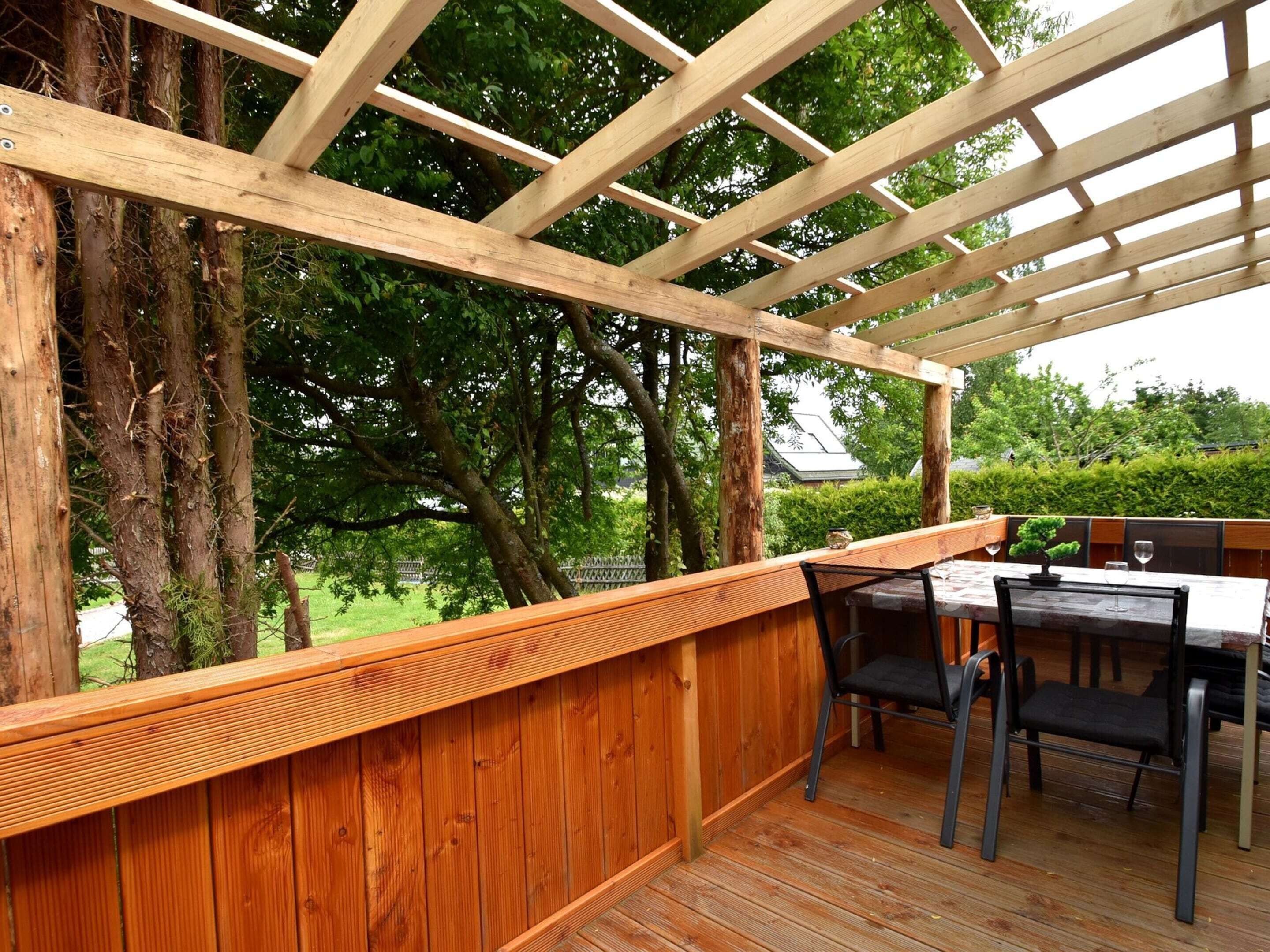 Un patio al aire libre con vigas de madera, baranda de madera y una mesa con sillas.