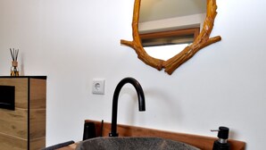 Un baño con lavamanos de piedra, grifo negro, tocador de madera y espejo con marco de madera.