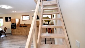 Una cocina moderna con armarios de madera, horno integrado y una ventana. Una escalera de madera apoyada contra la pared.
