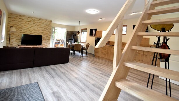 Una sala de estar moderna con una escalera de madera, un televisor de pantalla plana y un comedor con mobiliario de madera.